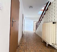 A hallway in a family house with brown tiles and a staircase.