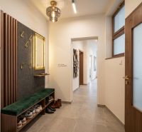 A hallway in a 3-room apartment with green plants, coat racks, and shoes on a bench.