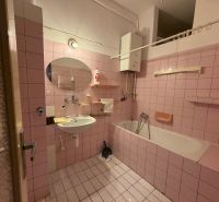 A bathroom with pink tiles, a bathtub, and a mirror in a 3-room apartment.