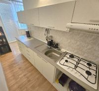 A kitchen with a gas stove and cabinets in a studio apartment, floor with wood decor.