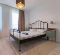 A bright bedroom with a metal bed, a lamp, and a floor with a wooden decor in a 2-room apartment.