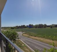 View from the balcony on Zuzana Chalupová Street, Bratislava - Petržalka, with a road and greenery.