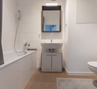 Bathroom with a bathtub, sink, mirror, and light tiles in a 2-room apartment.