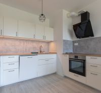 A kitchen in a 2-room apartment with a white kitchen unit and a floor with a wood decor.
