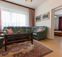 A living room with a wood-patterned floor, a green sofa, and an oriental rug in a three-room apartment.