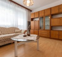 Living room in a three-room apartment with a wooden decor floor, a sofa, and a furniture set.