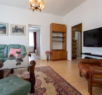 A living room of a three-room apartment with a wooden decor floor, a sofa set, and a television.