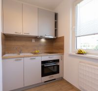 A kitchen in a 2-room apartment with wooden decor and fruit by the window.