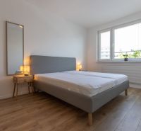 A bedroom in a two-room apartment with a wooden decor floor, a gray bed, and a nightstand.
