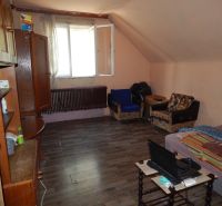 A room in a family house with a wooden decor floor, simple furnishings, and an open window.