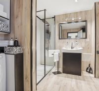 Bathroom in a 2-room apartment with a washing machine, shower, and floor with wood decor.