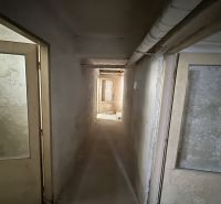 A narrow corridor with doors in commercial premises, plastered walls, older equipment.