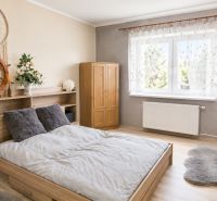 Bright bedroom in a family house with a bed, decorations, and a wooden-patterned floor.