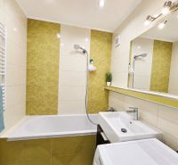 Bathroom with a bathtub, sink, and mirror, light tiles and decorative elements.