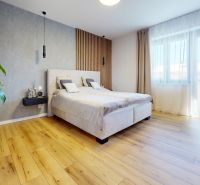 A bedroom in a three-room apartment with a bed, a plant, and a wooden decor floor.
