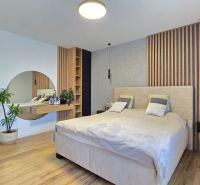 A bedroom in a 3-room apartment with a wood-patterned floor, a mirror, and plants.