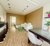 Living room with wood-patterned flooring, light furniture, part of a 3-room apartment.