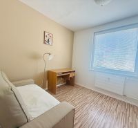 A room in a 3-room apartment with a sofa, a table, a wooden decor floor, and a large window.