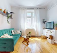 A bright living room with a sofa, wooden decor flooring, and plants in a three-room apartment.