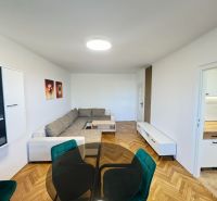 Bright living room with a sofa, wood-patterned flooring, and a kitchen in a 2-room apartment.