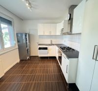 A kitchen in a 3-room apartment with white cabinets, a stove, and large windows, with a wooden decor floor.