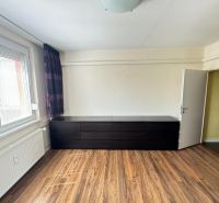 A bedroom in a 3-room apartment with a wood-patterned floor and a large dresser.