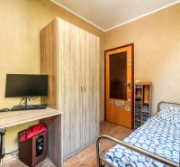 A room with a table, monitor, wardrobe, and bed, in a 4-room apartment, with a wooden decor floor.