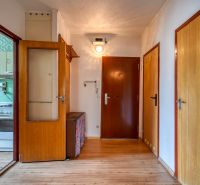 A hallway in a 4-room apartment with a wooden decor floor and a view of the kitchen.