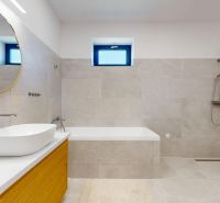 Bathroom with a bathtub and a sink in a family house, light ceramic tiles, large mirror.