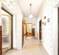 A hallway in a family house with patterned wallpaper, a display cabinet, and a door to the bathroom.