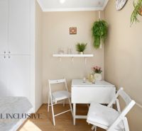 Dining area of a 3-room apartment with plants and white furniture, floor with wooden decor.