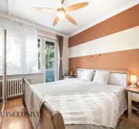 A bedroom in a 3-room apartment with a wood-patterned floor, a fan, and balcony windows.