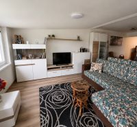 Living room with a colorful carpet, floral sofa, and wooden decor flooring.