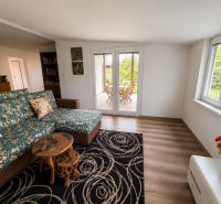 Living room in a cottage with a floral sofa, tables, and a view of the garden.