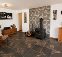 Interior of a cabin with a wood-burning stove, wooden decor flooring, wooden furniture, and decorations.