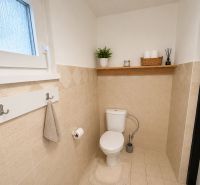 A bathroom in a cabin with beige tiles and a wooden shelf above the toilet.