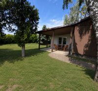 A cottage in Kopčany with a garden, terrace, and wooden furniture against a backdrop of greenery.
