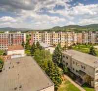 A view of the apartment buildings from Brezno on 9th May Street, surrounded by greenery and mountains.