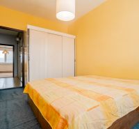 Bedroom with orange walls and a bed in a 3-room apartment, passage to the hallway.