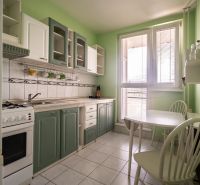 A kitchen in a 3-room apartment with white appliances, a green wall, and a dining table.
