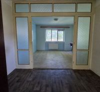 A living room in a three-room apartment with a wooden decor floor and glass doors.
