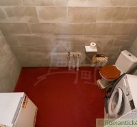 A bathroom in a cabin with older equipment, a washing machine, and a toilet.