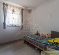 A room in a cottage with a bed and flowers on the windowsill, a floor with a wooden decor.