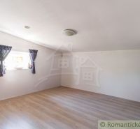 A spacious room in a cottage with a wooden decor floor and a window with blue curtains.