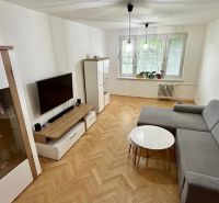Living room with wood-patterned flooring, gray sofa set, and television in a three-room apartment.