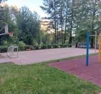 A playground with a basketball hoop and climbing frames in Banská Bystrica, surrounded by greenery.