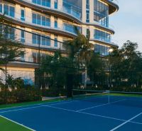 A tennis court in front of a modern building in Paje surrounded by greenery and palm trees.