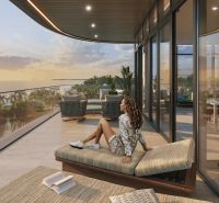 A woman is sitting on the terrace of a studio apartment with an ocean view at sunset.