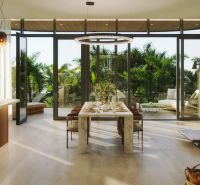 Modern dining room with luxurious table setting, view of the terrace, and wooden decor flooring.