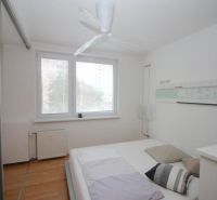A bright bedroom with a large window and a wooden decor floor in a 3-room apartment.